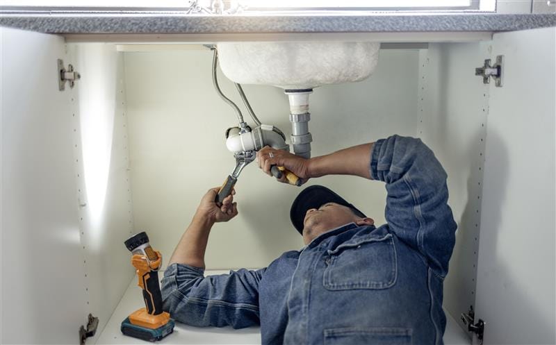 Plumber repairing pipes beneath a bathroom sink in Coachella
