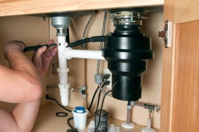 Plumber repairing a garbage disposal beneath a kitchen sink in Coachella