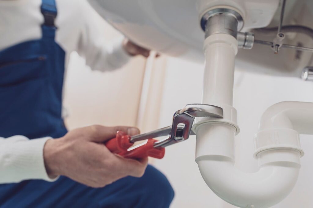 Plumber repairing a white drain pipe beneath a sink in Coachella