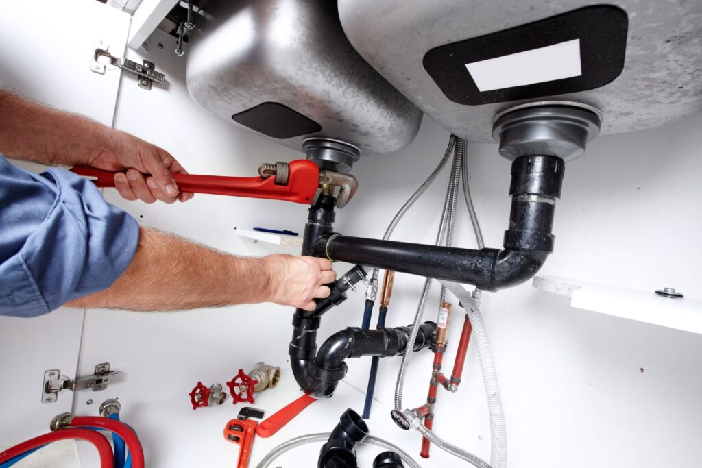 Plumber repairing drain pipes beneath a kitchen sink in Coachella
